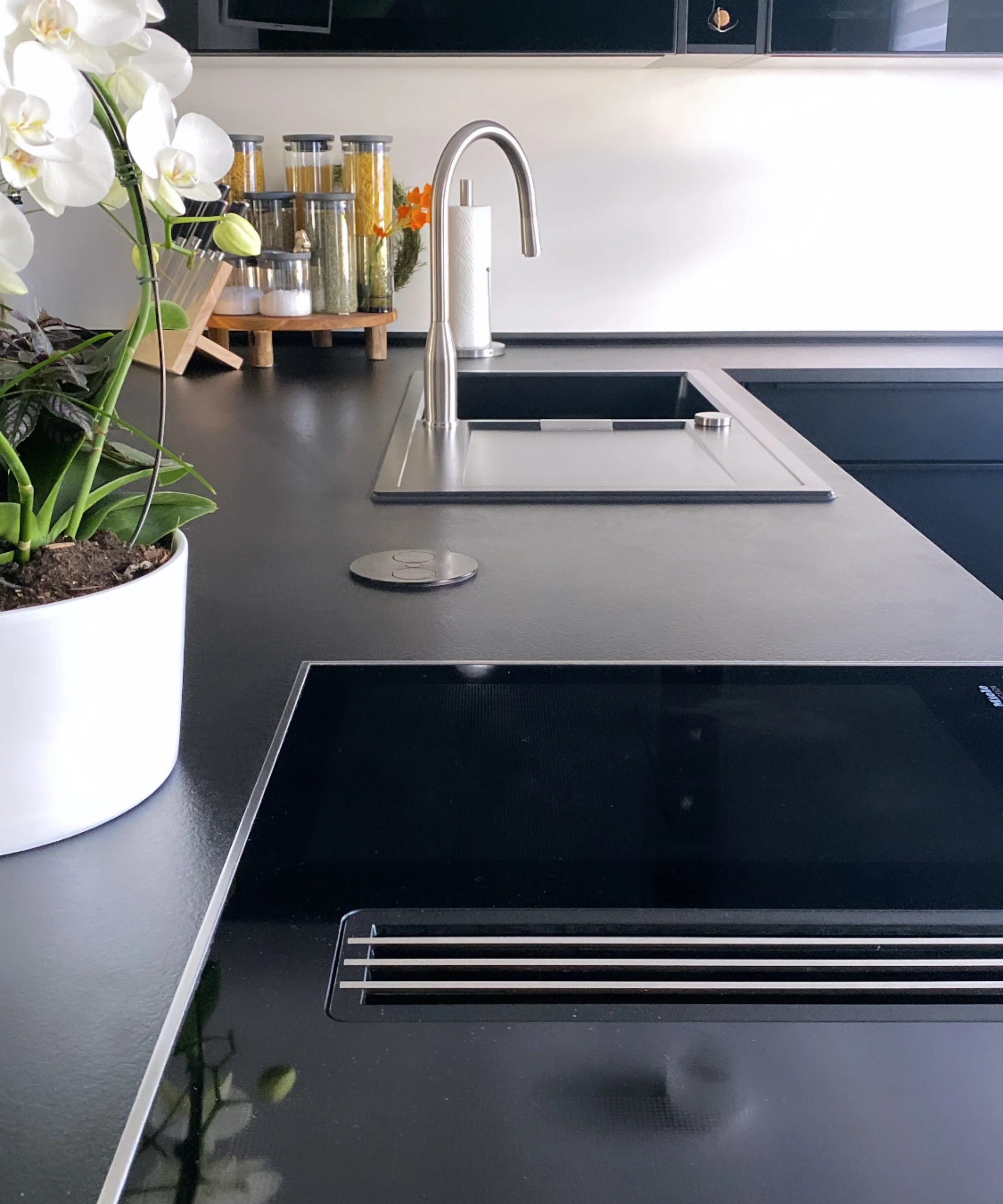 Eine moderne Küche mit schwarzer Arbeitsplatte und weißen Orchideen, Nolte Küchen.