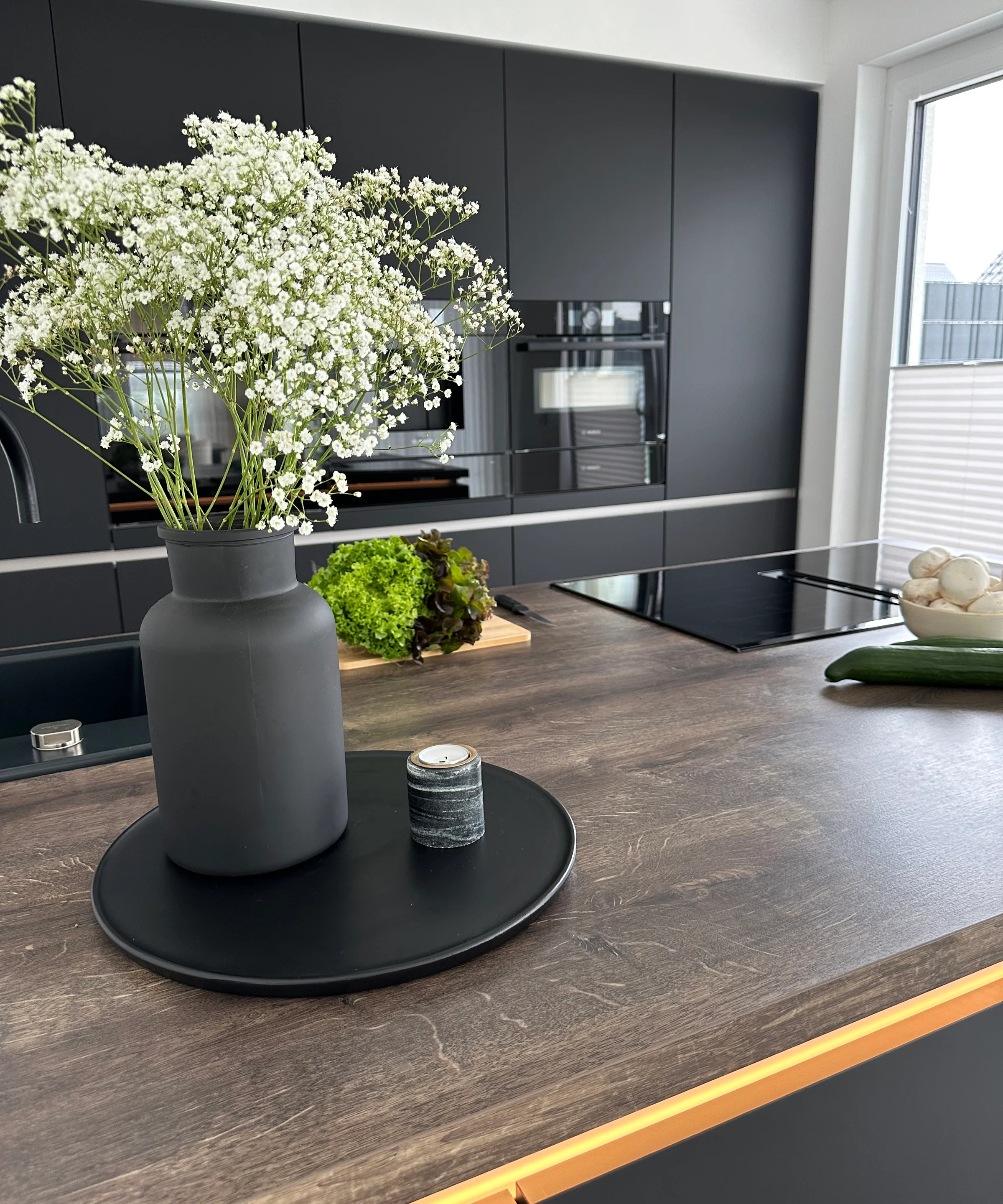 In einer modernen Küche mit dunklen Schränken steht eine Vase mit Blumen auf der Arbeitsplatte. Nolte Küchen.