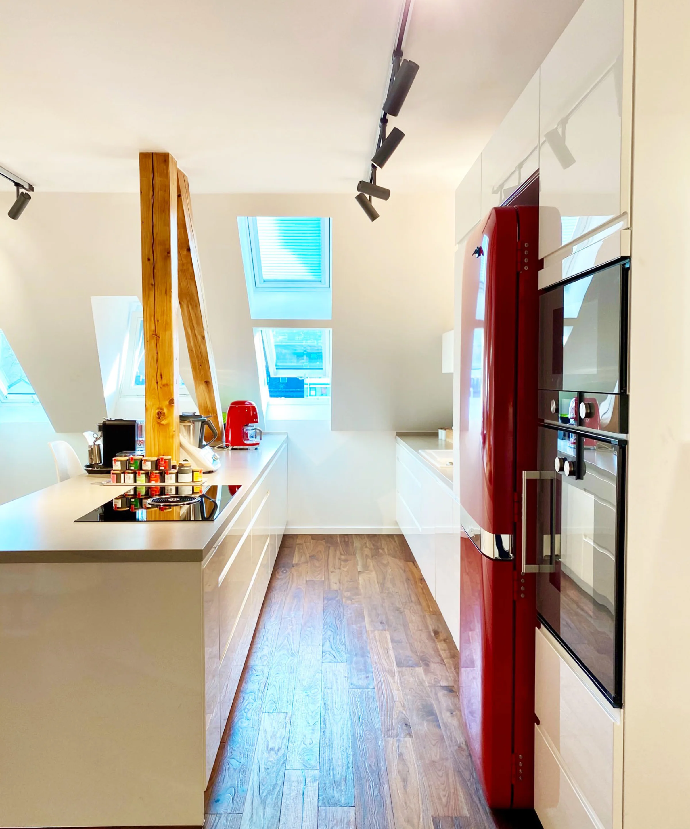 Eine moderne Küche mit roten Akzenten und Holzelementen, beleuchtet durch Dachfenster. Nolte Küchen.