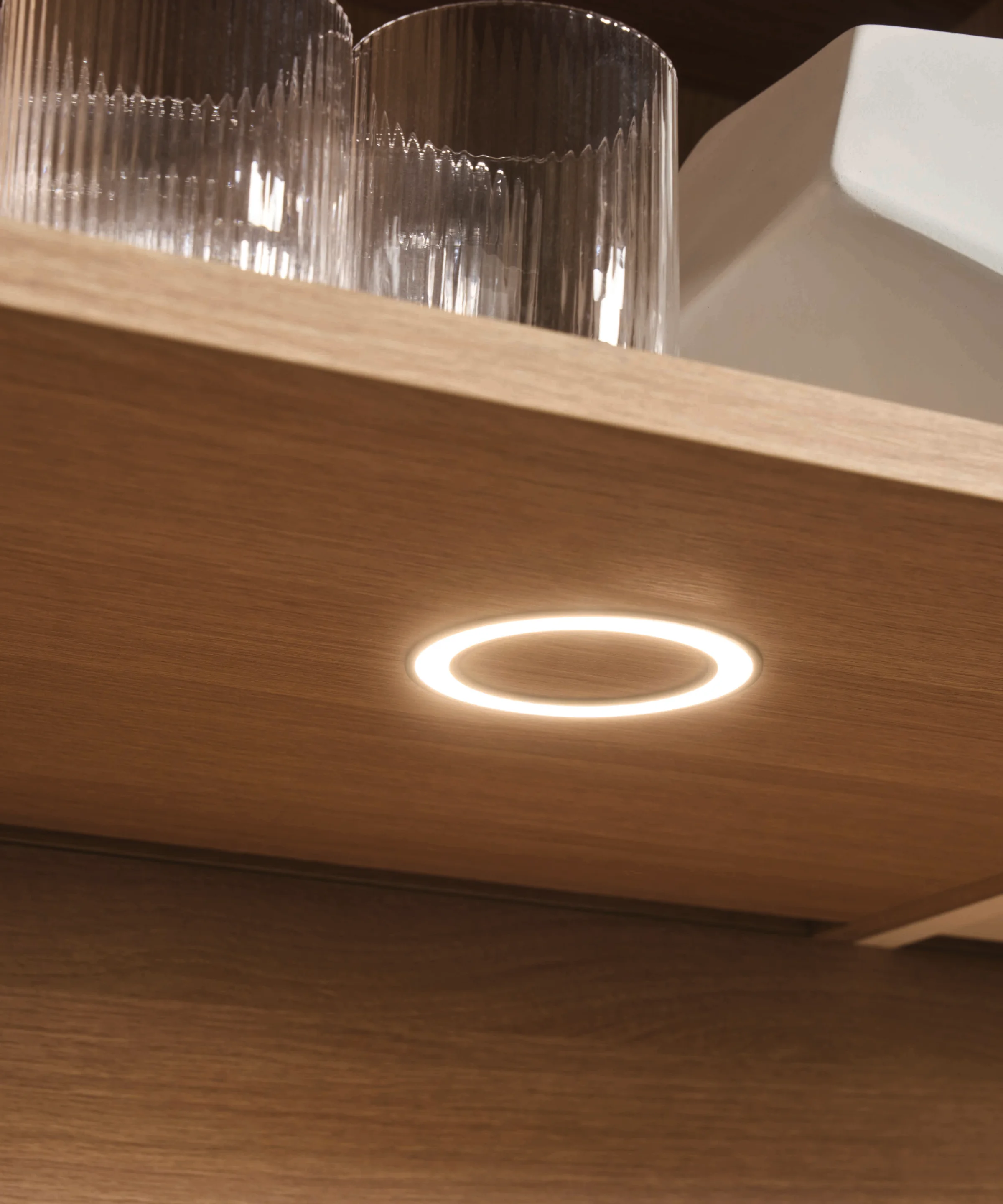 Ein beleuchteter Holz-Küchenschrank mit Gläsern und einer weißen Schale. Express Küchen.