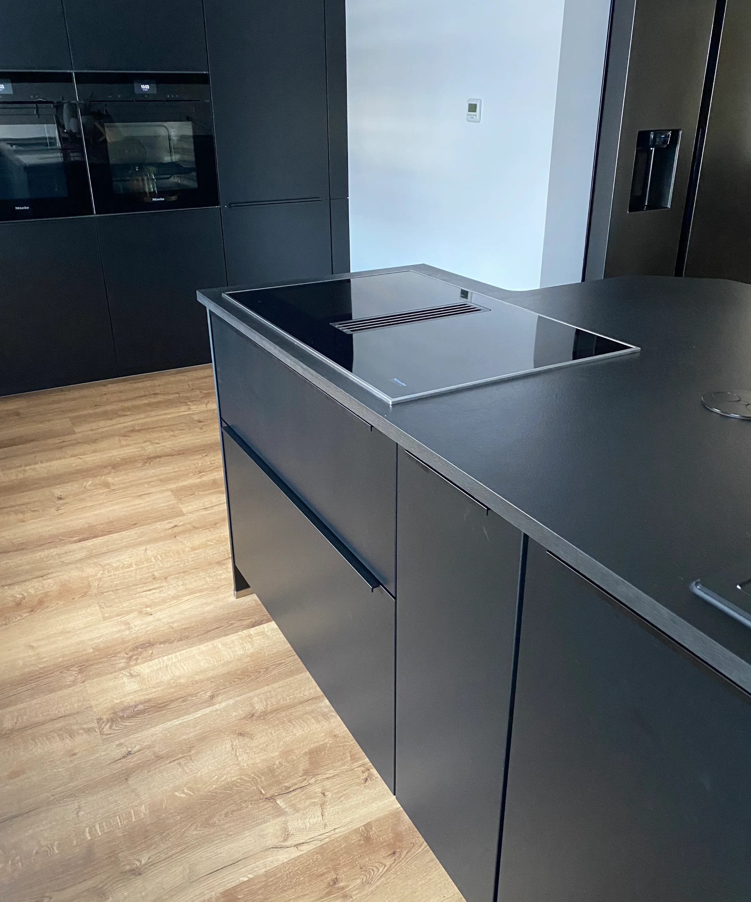 Eine moderne Küche mit schwarzem Design und Holzfußboden, ausgestattet mit Nolte Küchen.