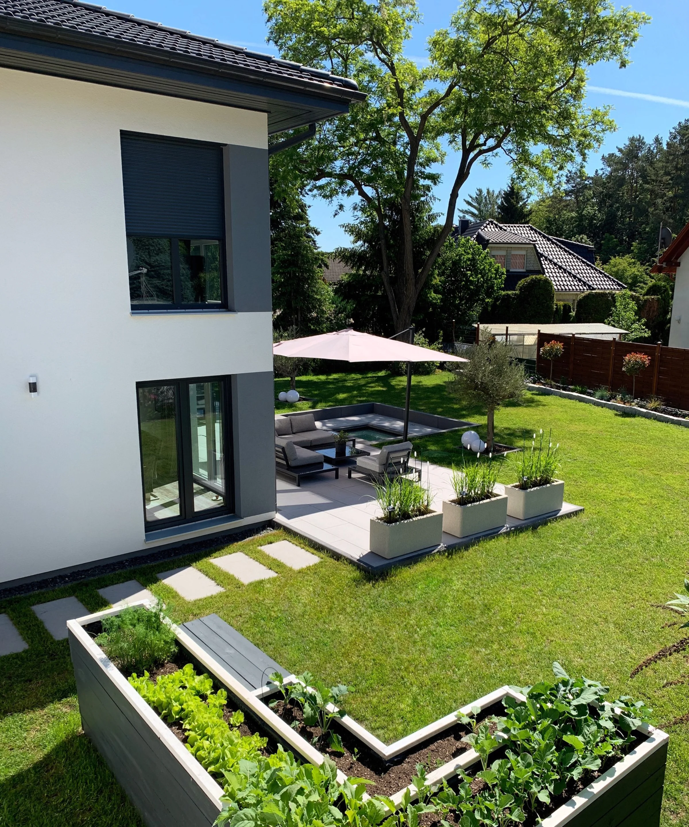 Ein moderner Garten mit Terrasse und Hochbeeten neben einem Haus.