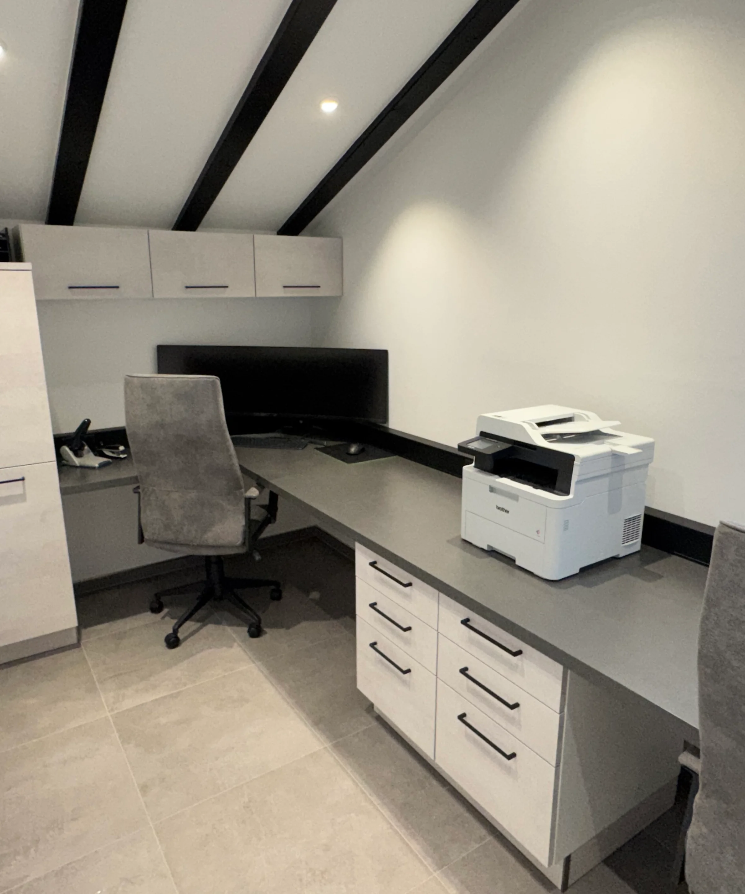 Ein modernes Arbeitszimmer mit Schreibtisch, Stühlen und Drucker unter einer Dachschräge. Nolte Living.