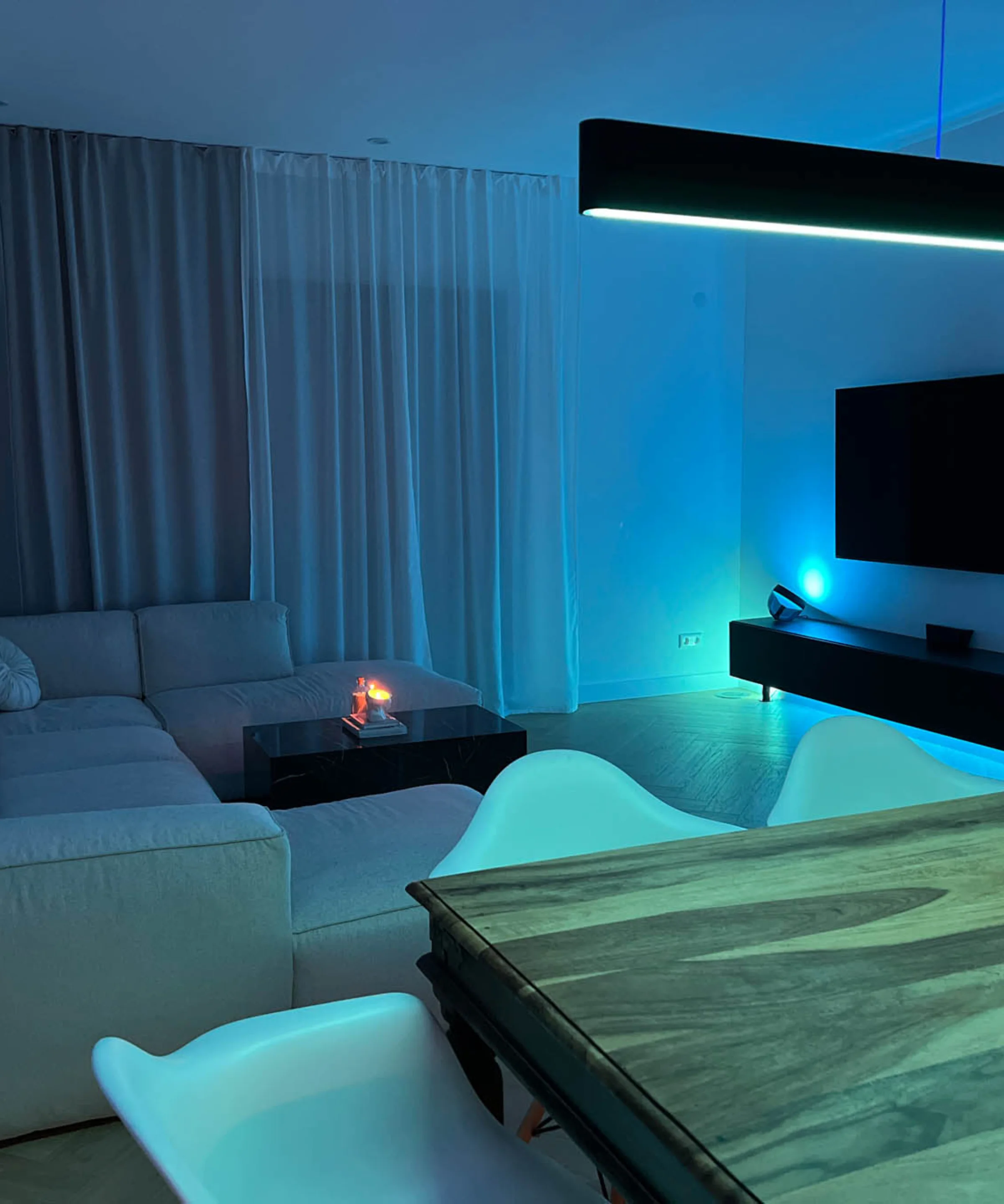 Ein modern beleuchtetes Wohnzimmer mit Sofa und Esstisch, ergänzt durch Nolte Living.