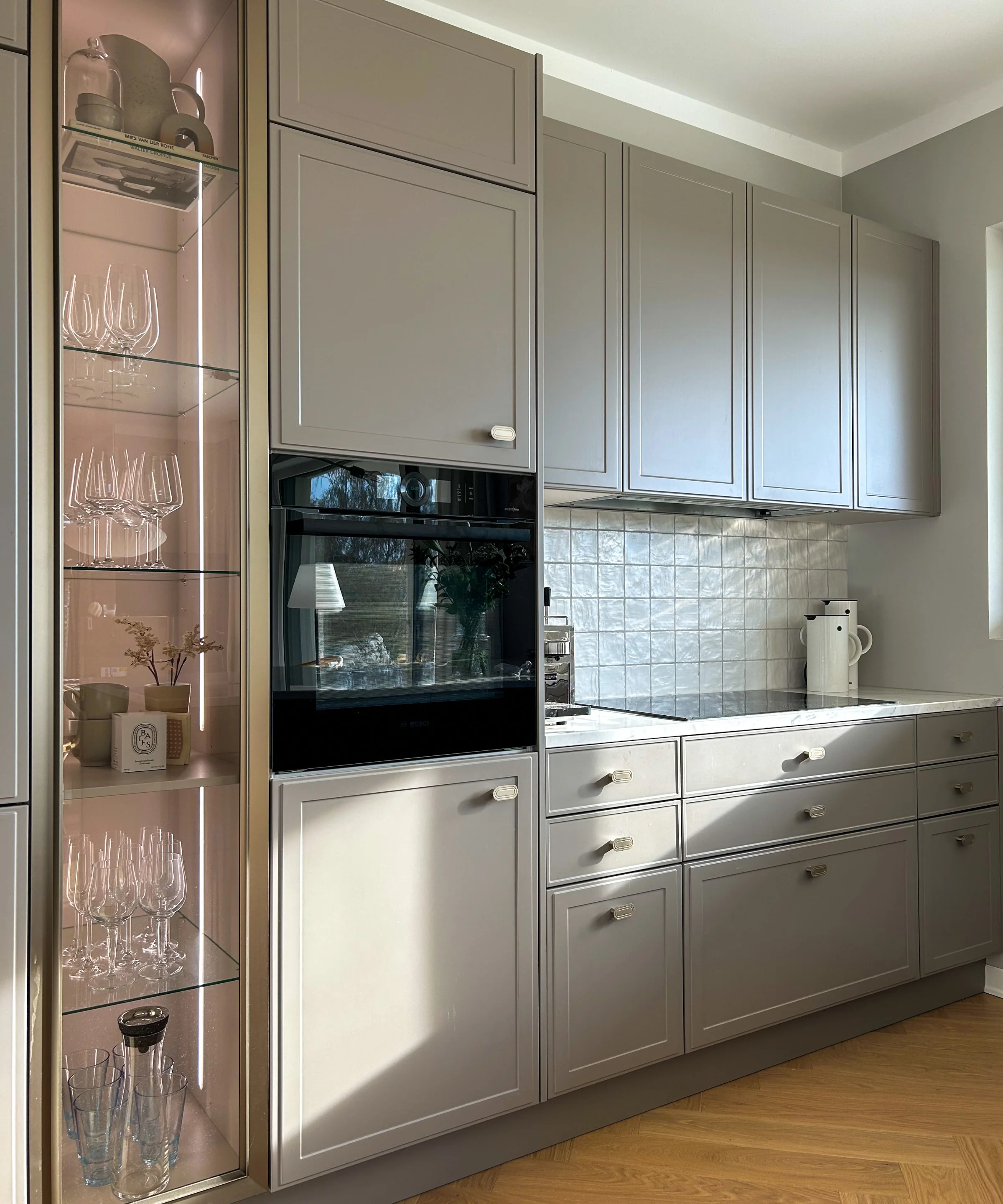 A modern kitchen with gray cabinets and a glass display, presented by Nolte Kitchen.