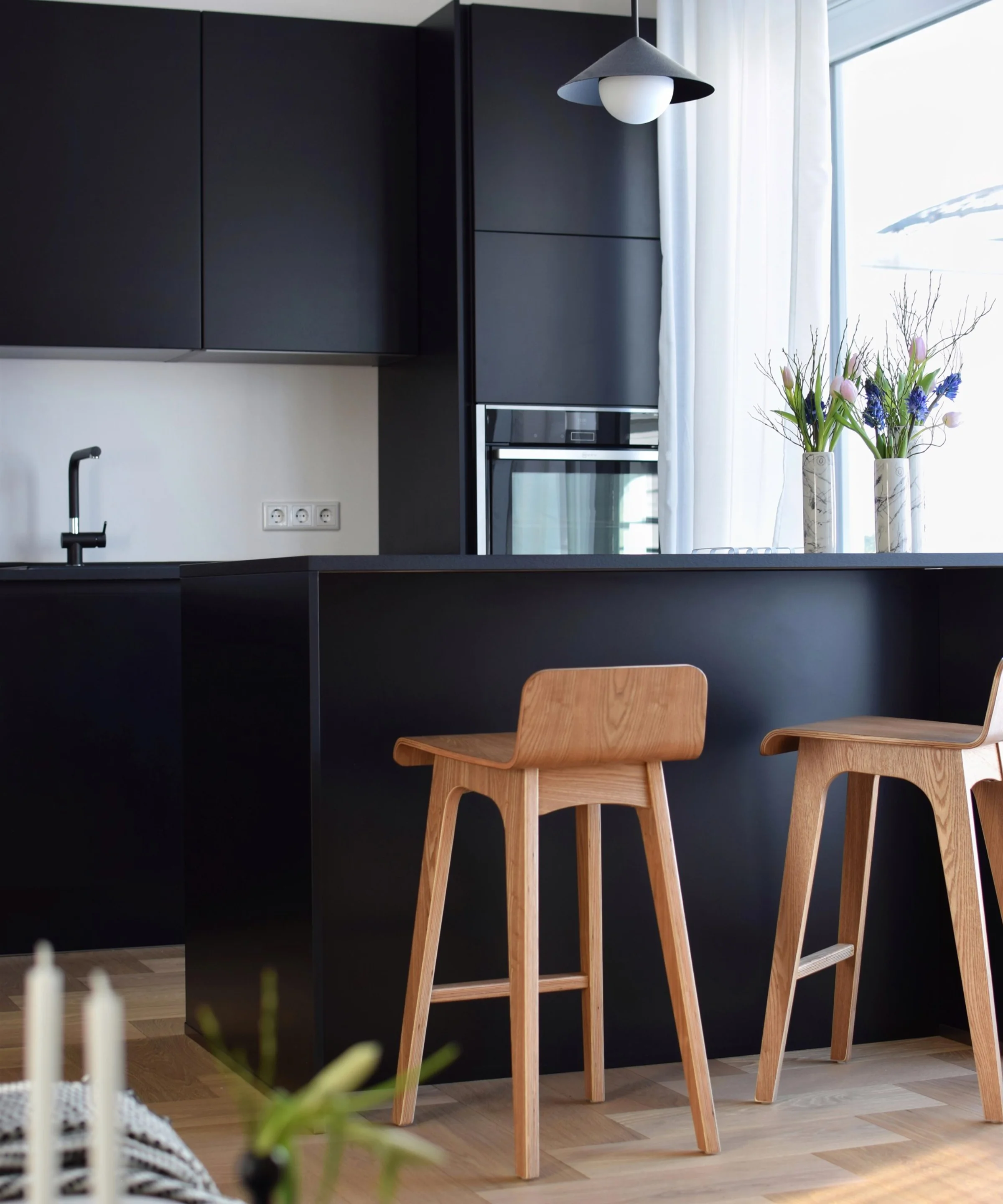 A modern kitchen with black cabinets and wooden chairs, designed by Nolte Kitchen.