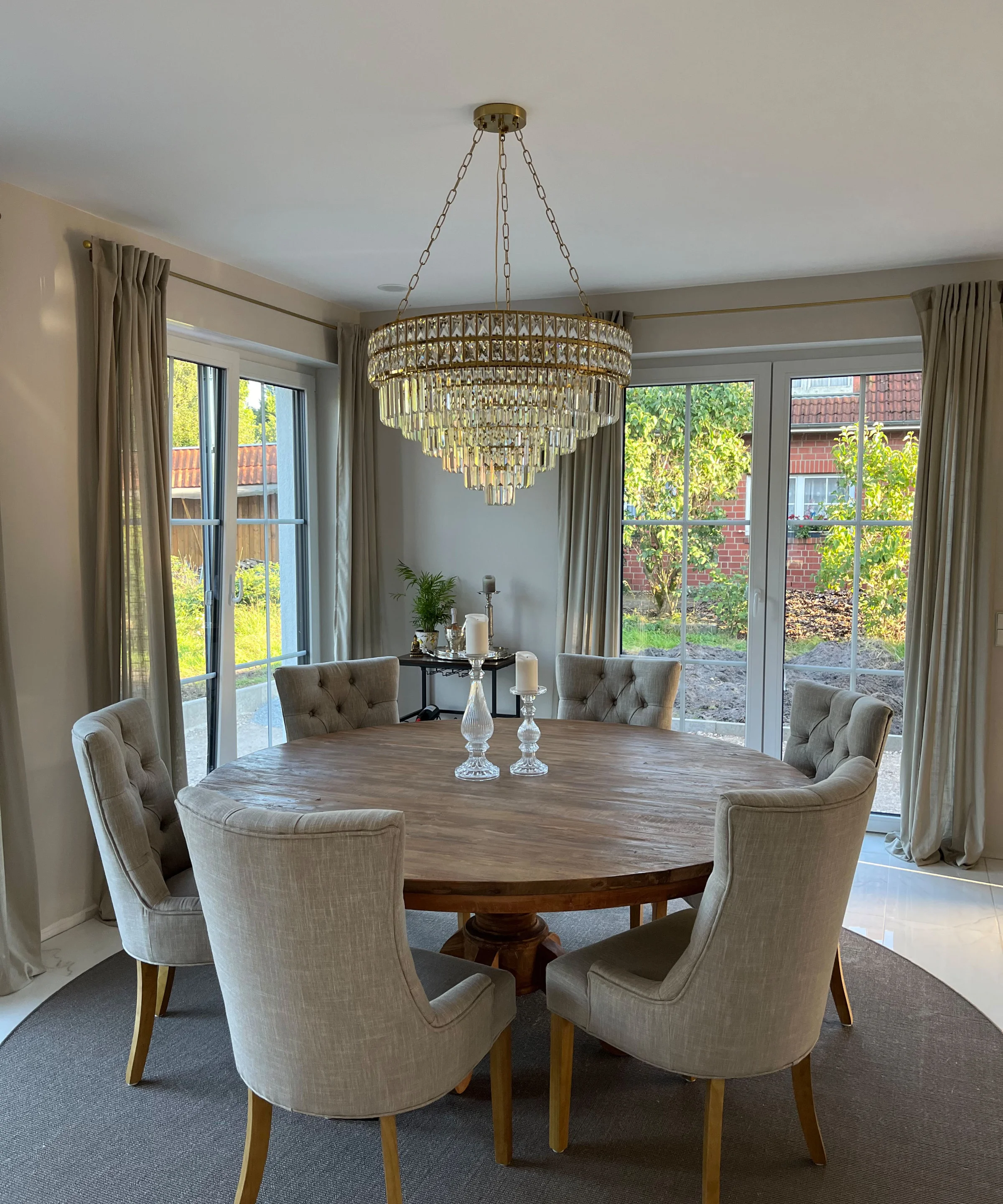 Ein eleganter Essbereich mit rundem Holztisch und Polsterstühlen unter einem Kronleuchter. Nolte Living.
