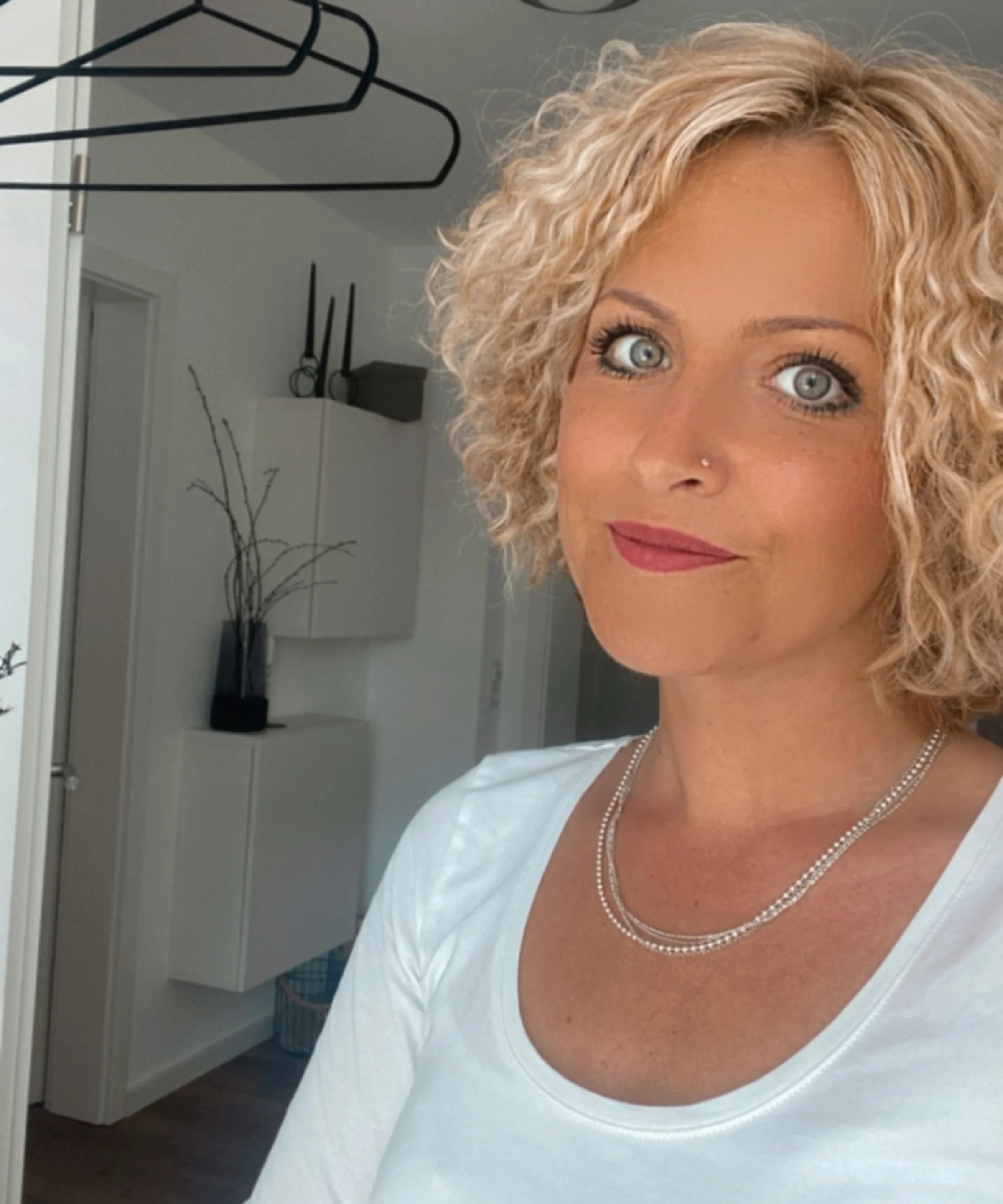 Eine Frau mit lockigem blondem Haar steht in einem modern eingerichteten Raum.