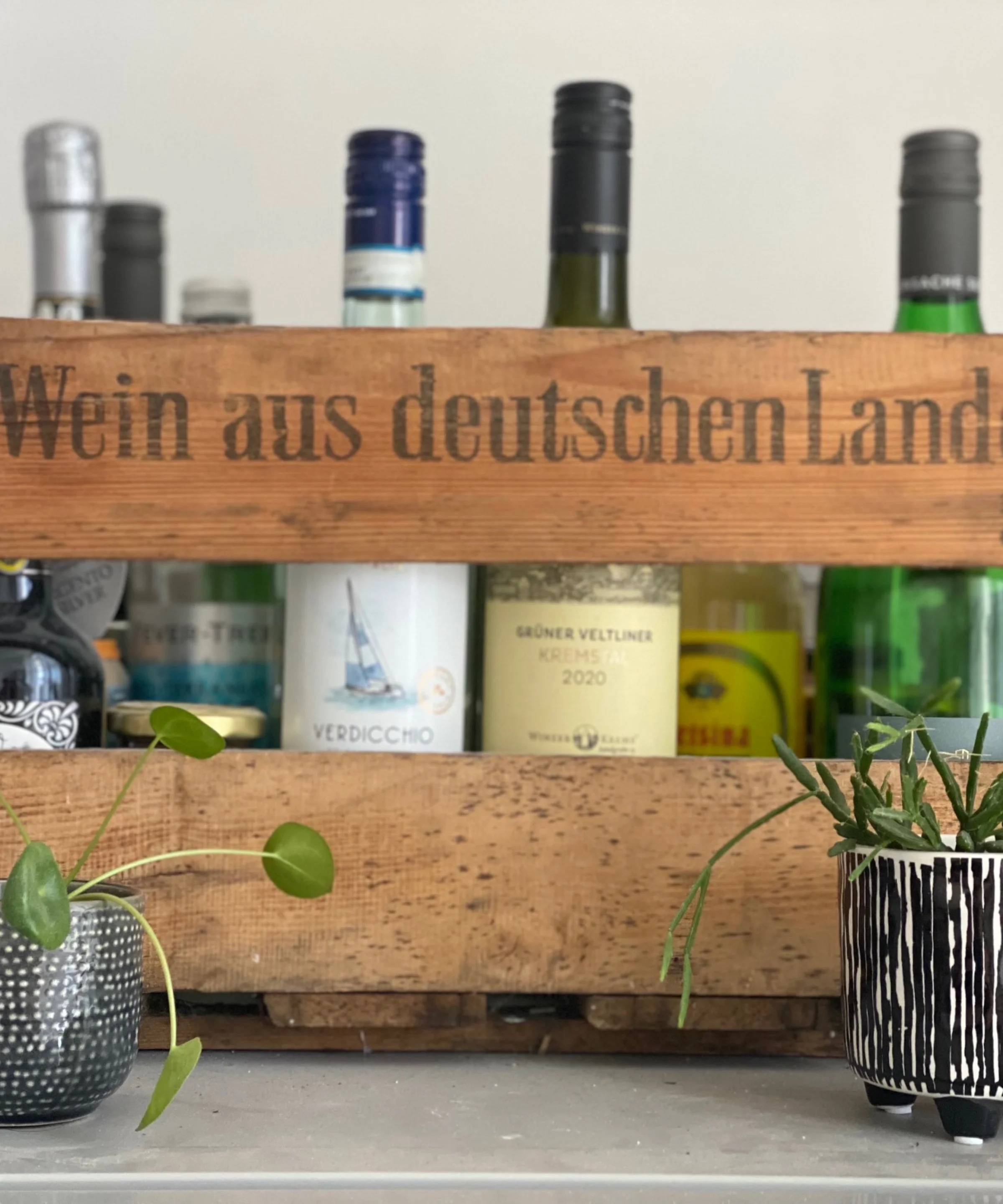 Eine Holzkiste mit Flaschen und Pflanzen vermittelt ein stilvolles Ambiente, passend zu Nolte Küchen.
