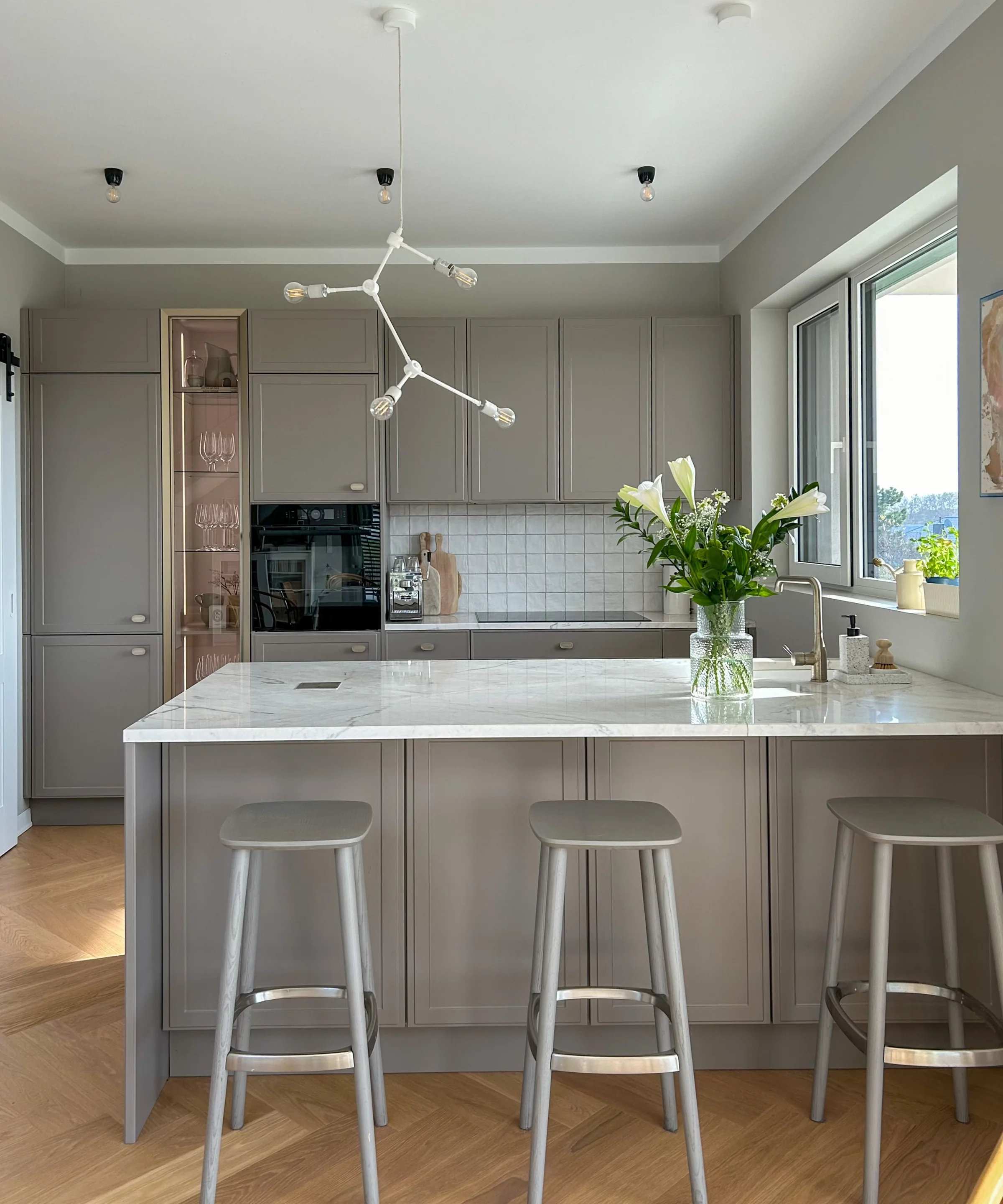 A modern kitchen with gray cabinets and an island, decorated with flowers. Nolte Kitchens.