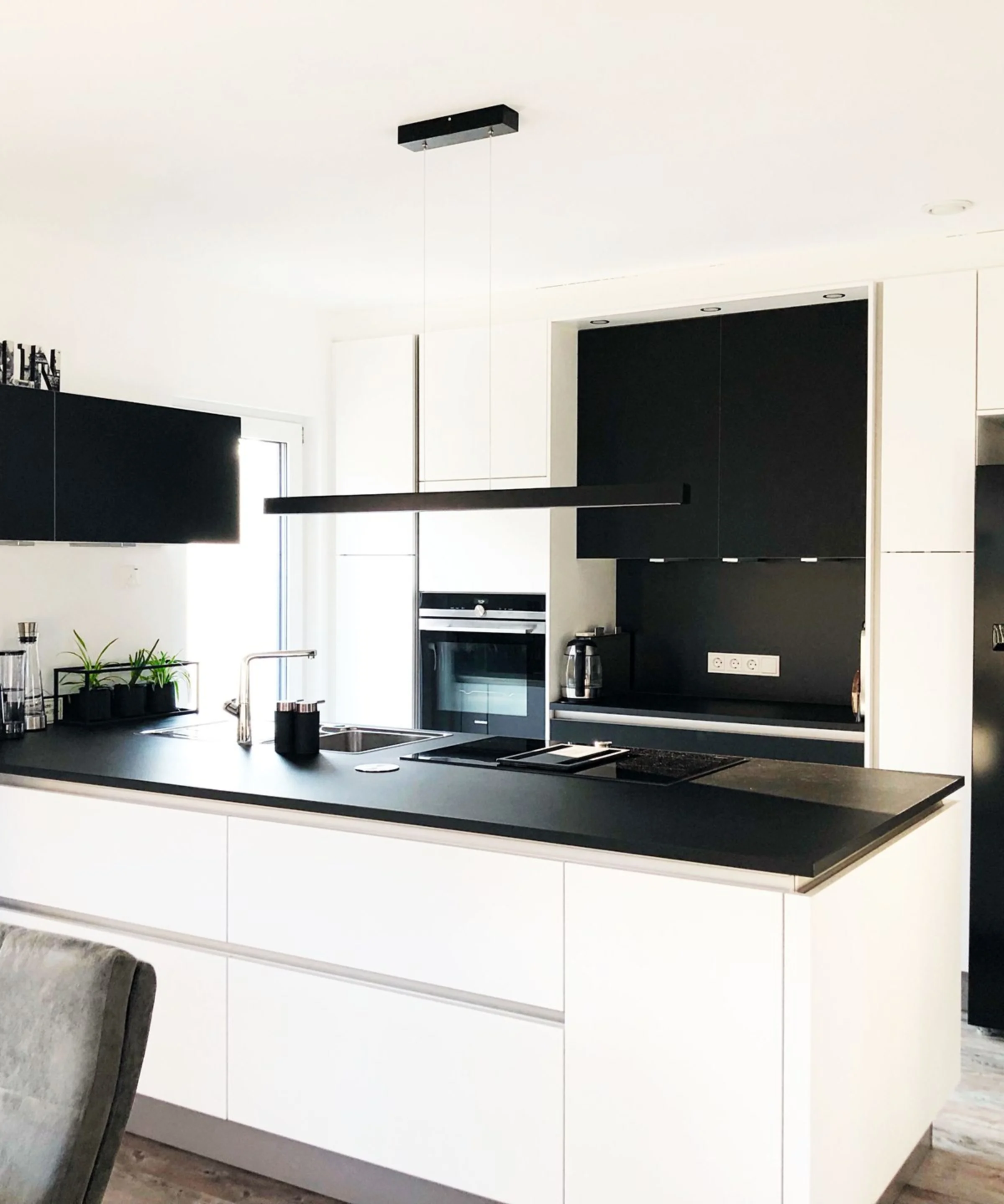 Eine moderne, schwarz-weiße Küche mit Insel und Hängelampen, gestaltet von Nolte Küchen.
