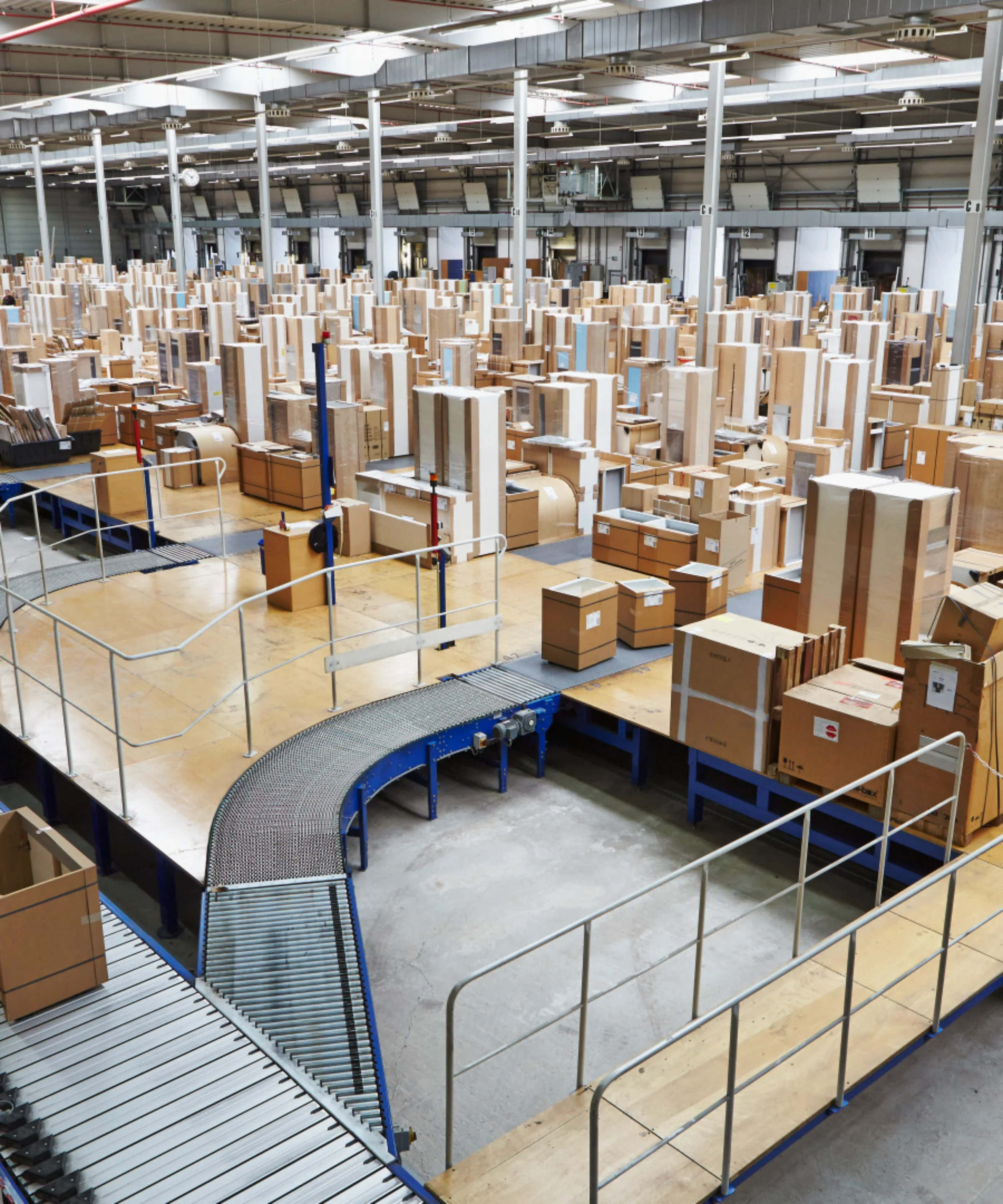 In a large warehouse, numerous packaged wooden parts are on conveyor belts.