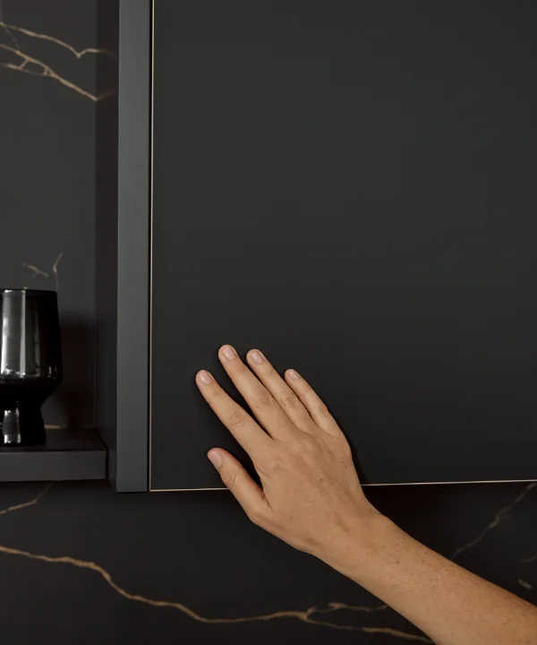 Eine Hand berührt einen eleganten schwarzen Küchenschrank. Nolte Küchen.