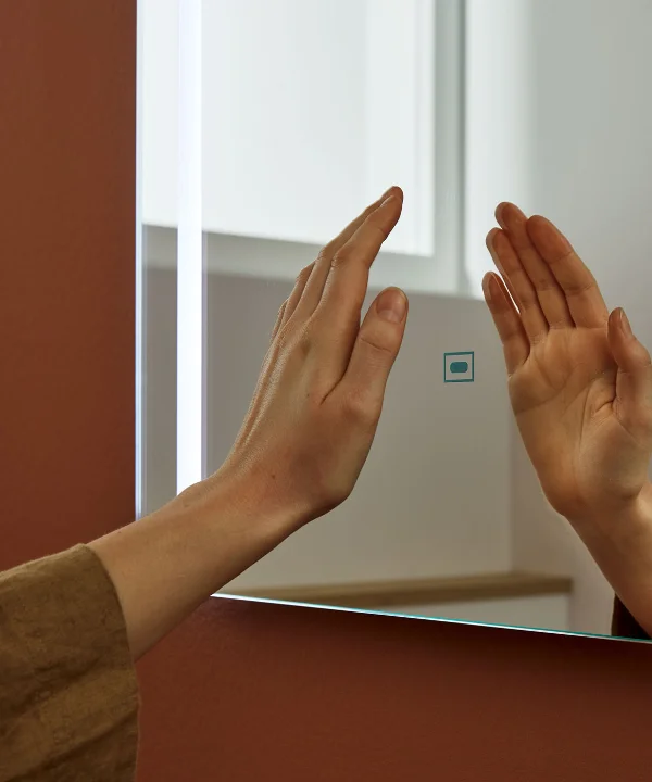 Eine Hand berührt einen beleuchteten Spiegel in einem modernen Badezimmer, Nolte SPA.