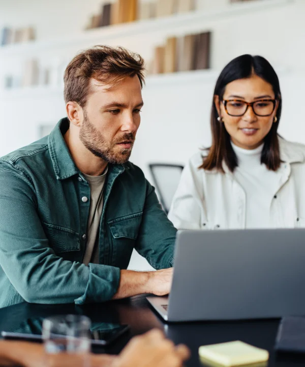 Drei Personen sitzen an einem Tisch und arbeiten gemeinsam an einem Laptop.